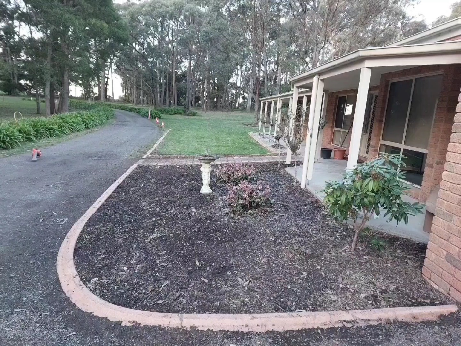 A new mulched garden bed with concrete edging beside a driveway